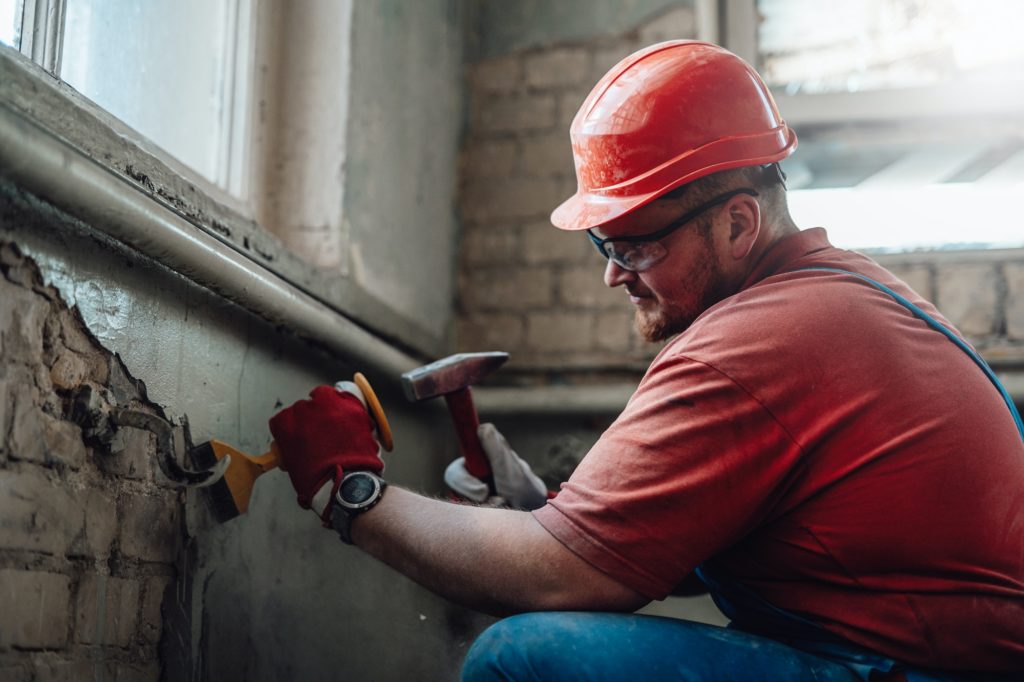 Builder on a construction site working on a brick wall with a hammer